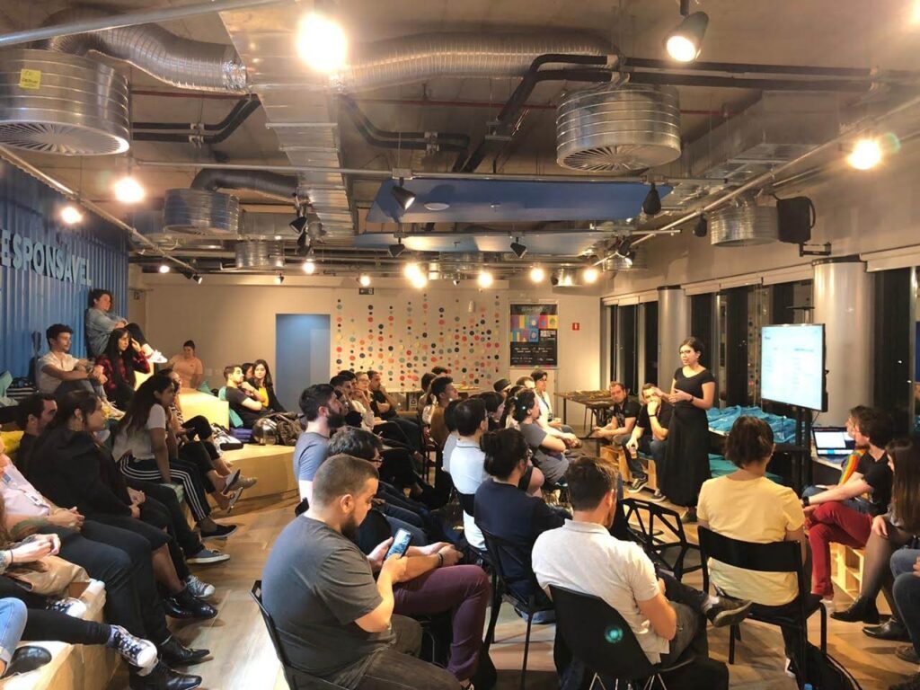 Thaís apresentando em um evento de tecnologia, com a plateia sentada ao redor