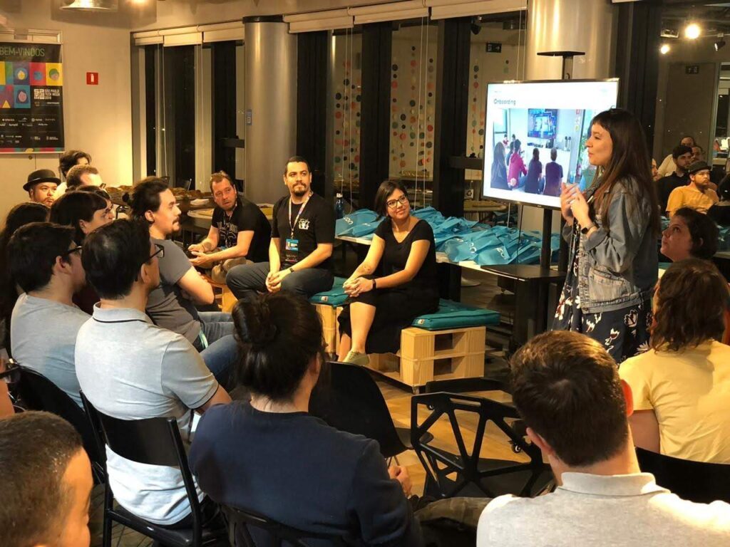Thaís apresentando um fluxo de onboarding em um meetup, com o público sentado à frente